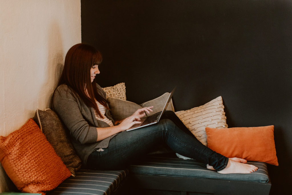 A woman lounges on a daybed while working on a laptop.Head to this post for the top 3 reasons to switch from Honeybook to Dubsado.